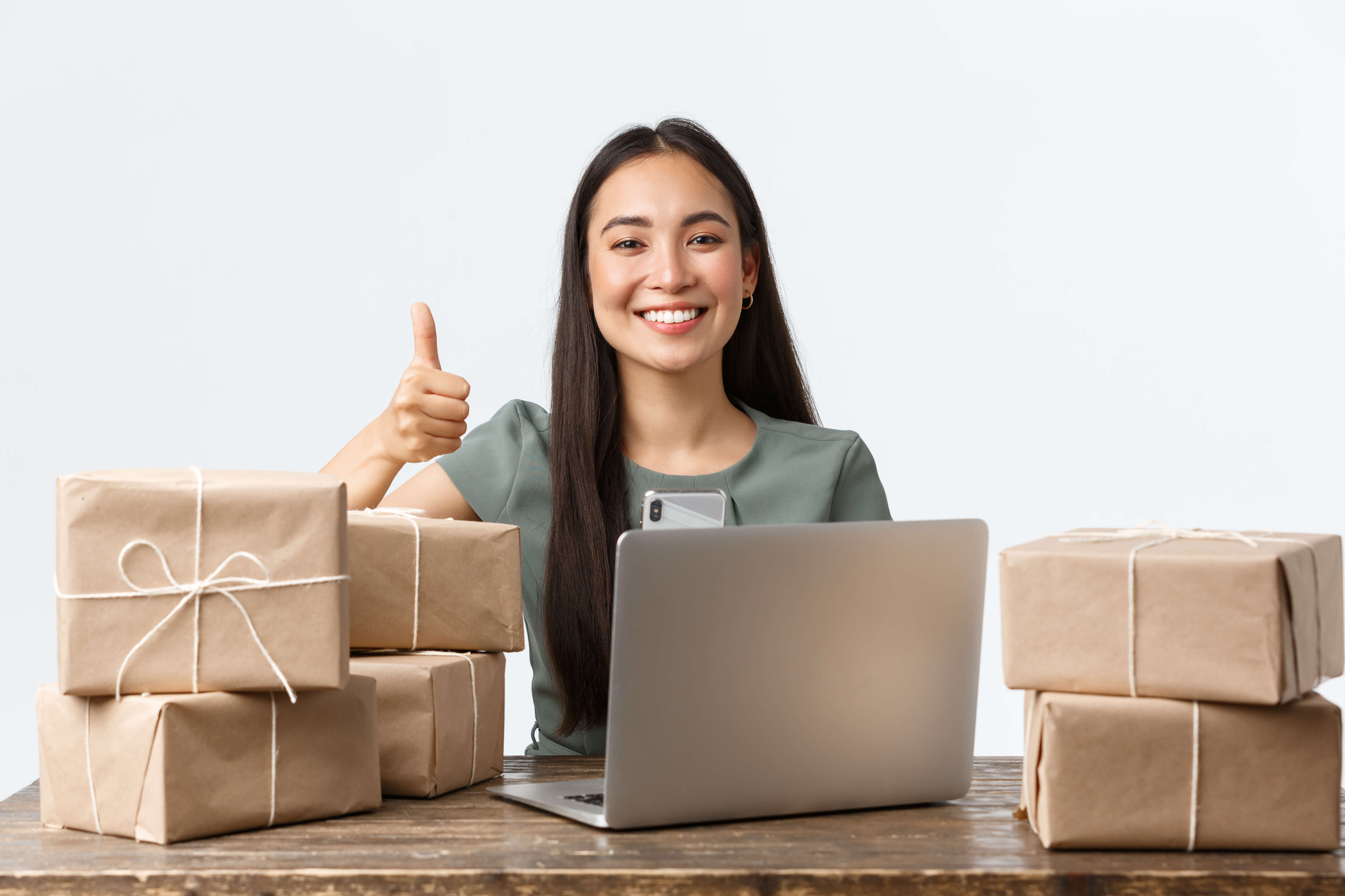 Small business owners, startup and e-commerce concept. Happy asian businesswoman with online shop, packing orders at home, show thumbs-up, manage clients requests via laptop, white background.