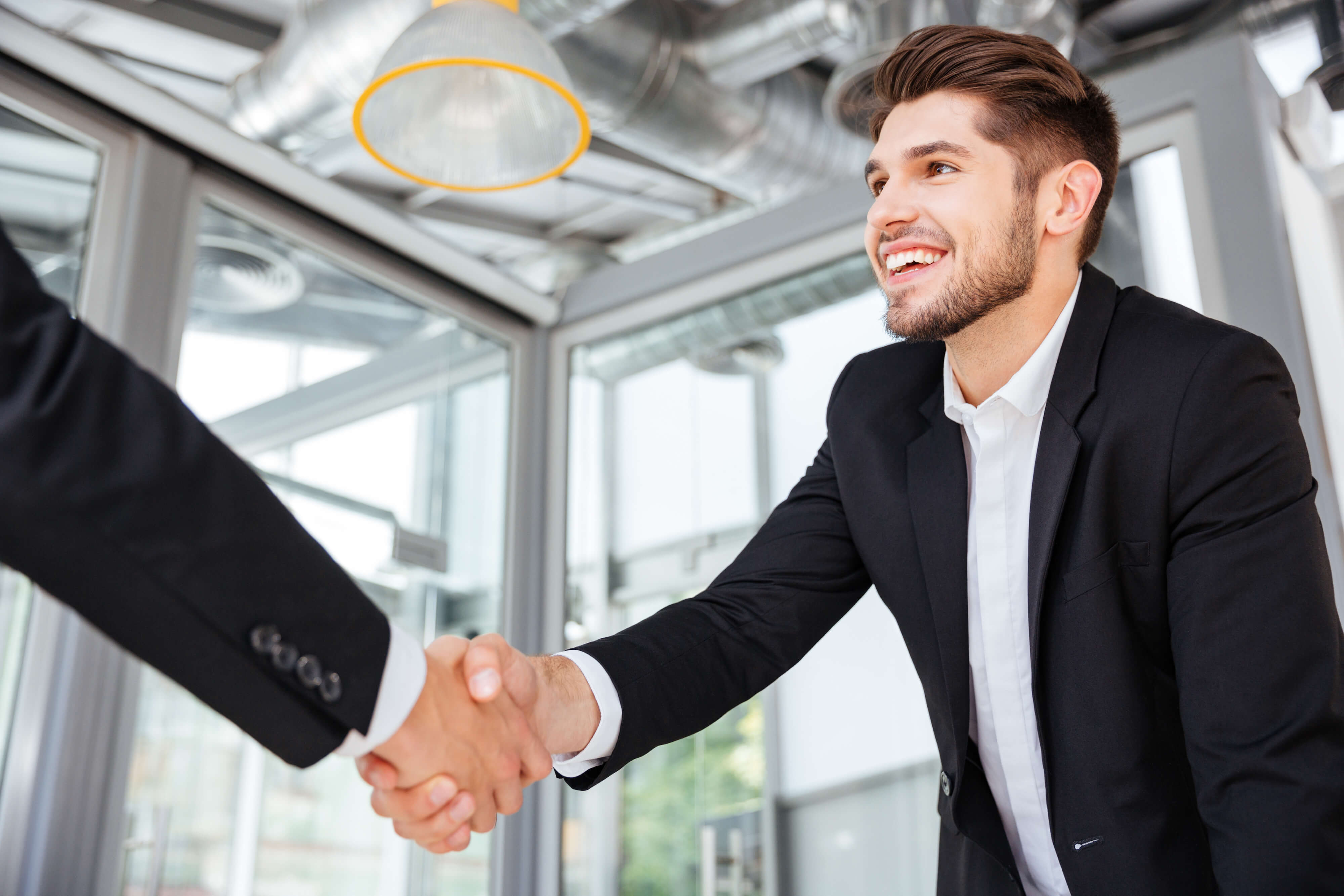 Two smiling successful young businessmen shaking hands on business meeting in office